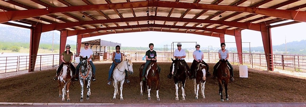 Group horseback riding lesson under covered arena.