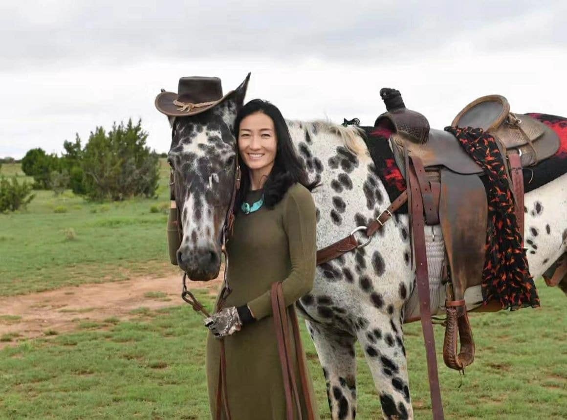 Woman with horse wearing cowboy hat in field.