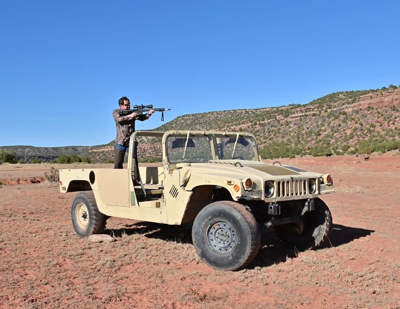 Person aiming rifle on vintage military jeep outdoors.