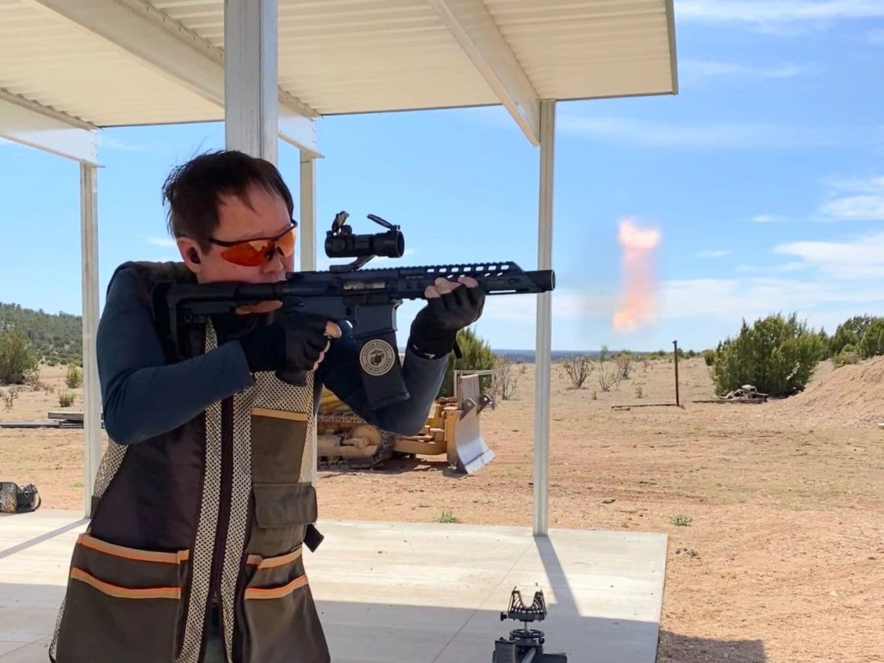 Person firing rifle at outdoor shooting range.