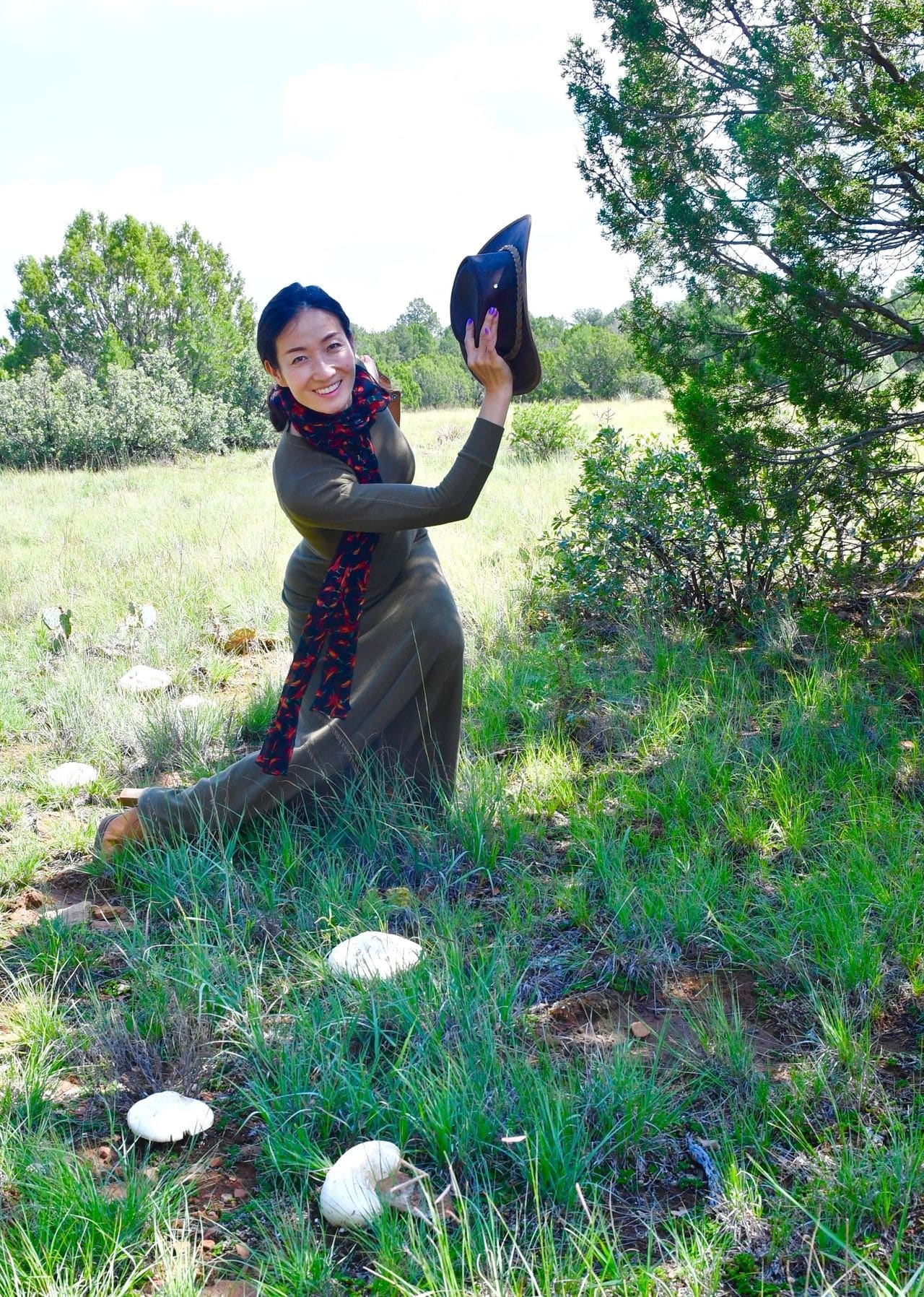 Woman smiling, holding hat, outdoors near mushrooms.