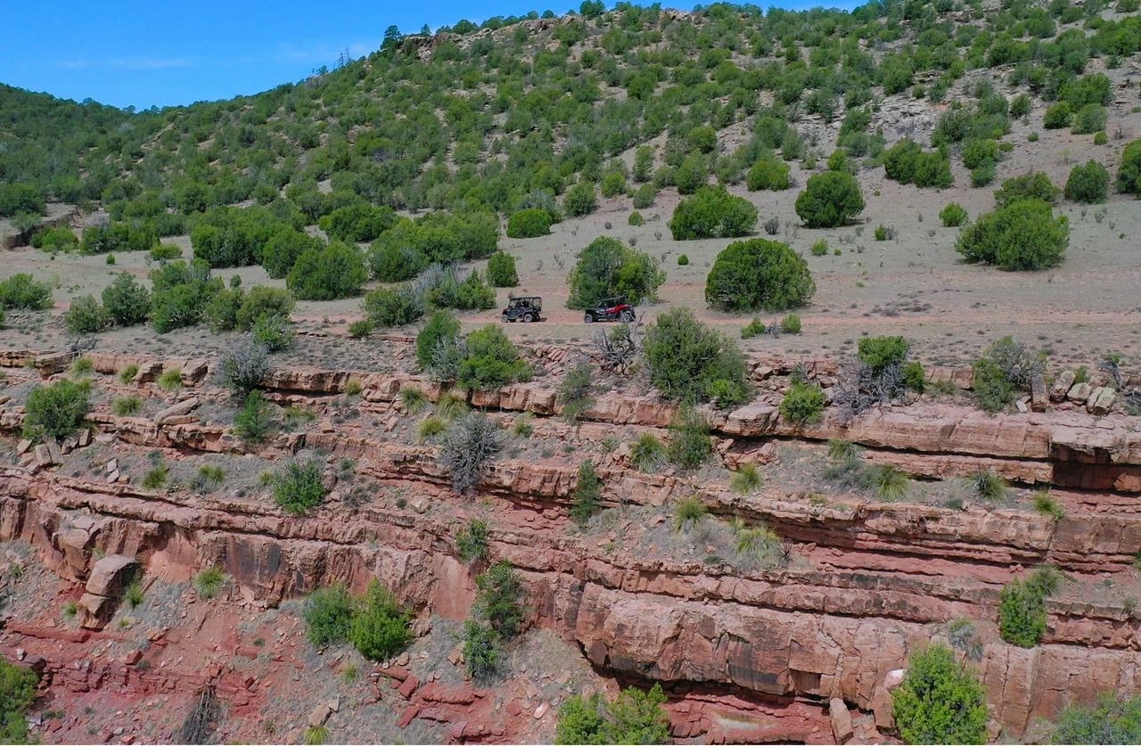 Off-road vehicles on desert canyon cliff edge.