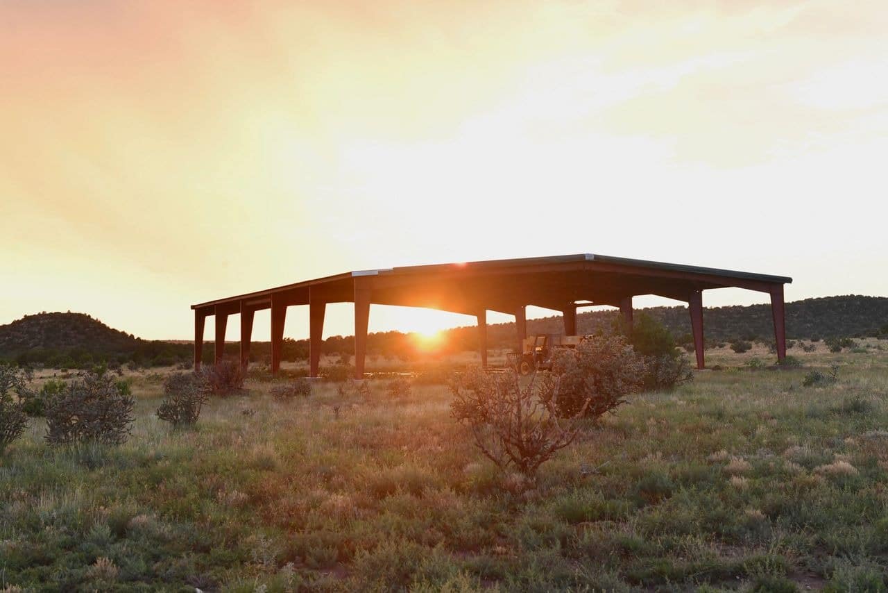 Sunset behind rustic open-air structure in desert landscape.