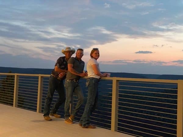 Three people watching sunset from scenic lookout.