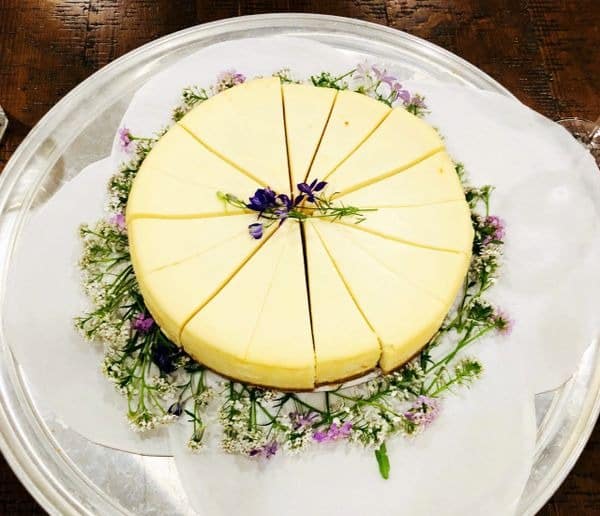 Sliced cheesecake with edible flowers on glass plate.