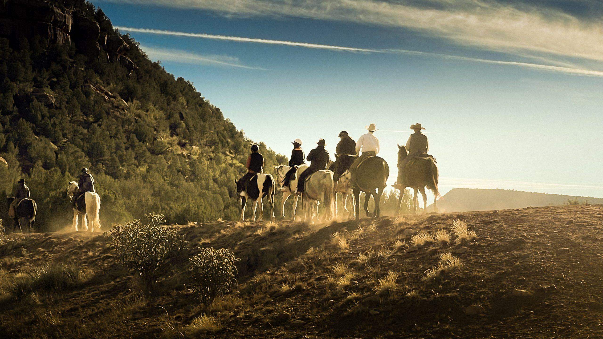 Horseback riders on trail at sunset in nature.